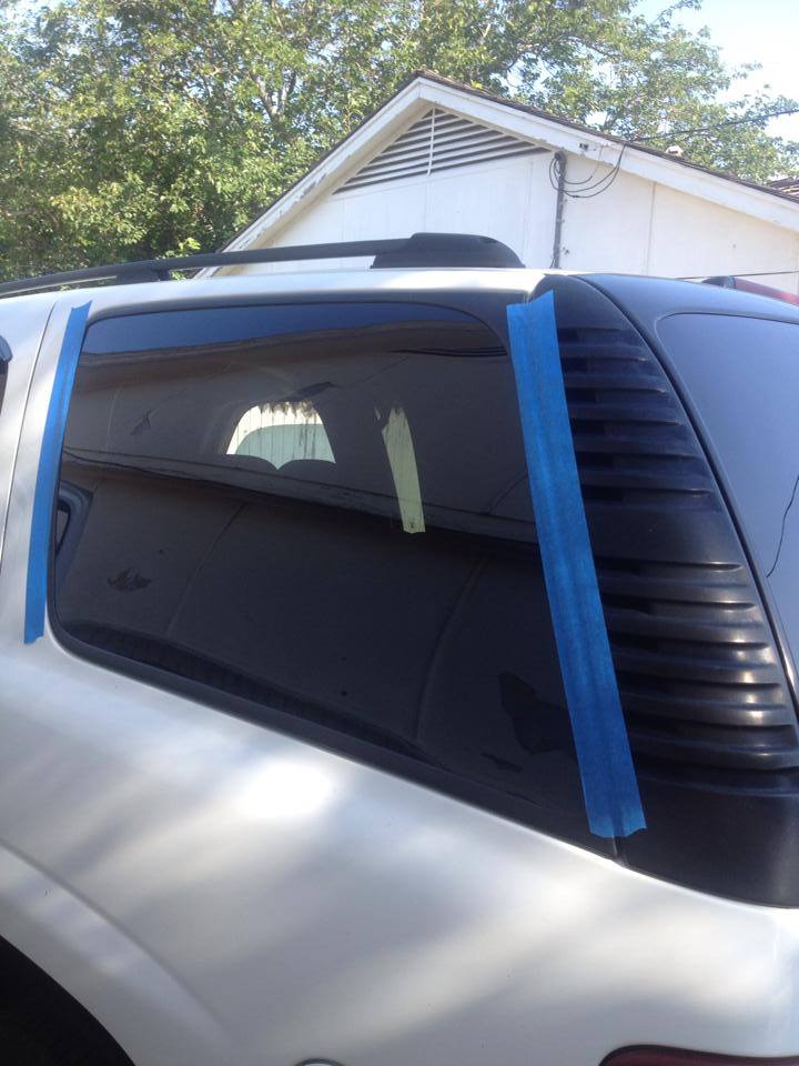 A car with blue tape applied to its window, indicating a temporary repair or covering.