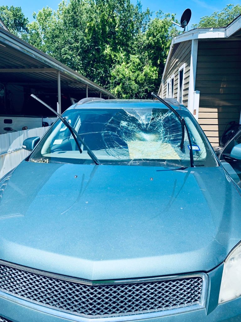 A car with a shattered windshield parked on the side of the road, indicating damage and potential safety concerns.